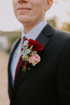 a man in a suit and tie with flowers on his lapel flower is looking at the camera