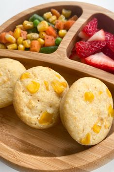 three biscuits are on a wooden plate with strawberries, corn, and carrots