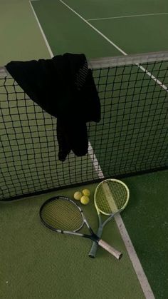 a tennis racket and ball on the ground next to a net with clothes hanging over it