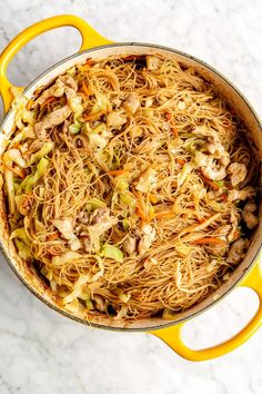 a yellow pot filled with noodles and vegetables on top of a white countertop next to an orange spatula