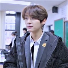 a young man wearing a jacket and tie in a room with other people standing around