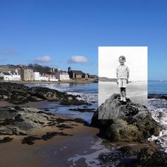 a black and white photo of a young boy standing on top of a rock near the ocean