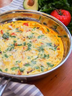 an omelet in a pan on a table with tomatoes, broccoli and cucumbers