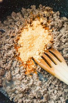 a wooden spatula with ground meat and seasoning in it next to a wooden spoon