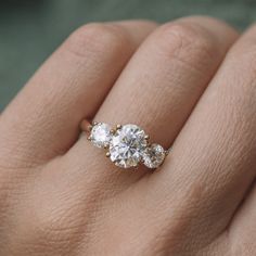 a woman's hand holding an engagement ring with three stones on top of it