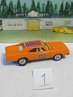 an orange toy car sitting on top of a table next to a number one sign