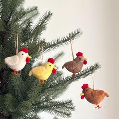 three ornaments are hanging from a pine tree with red and yellow roosters on them