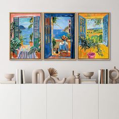 three paintings are hanging on the wall above a white cabinet with books and vases