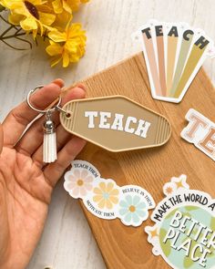 a person holding a keychain that says teach on it and some flowers in the background