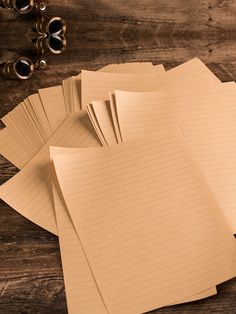 several lined papers on a wooden table next to some binoculars and an old pair of eyeglasses