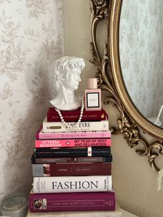 a stack of books sitting on top of a white table next to a gold framed mirror