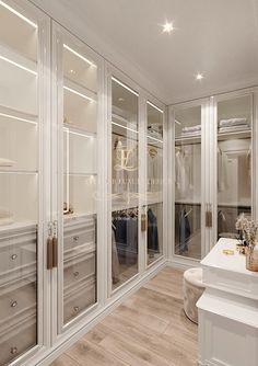 a large walk in closet filled with lots of white furniture and glass doors on the walls