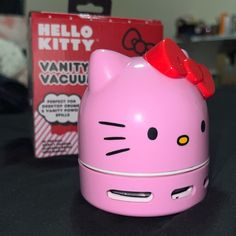 a pink hello kitty alarm clock with a red bow on it's head and an unopened box in the background