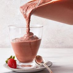 chocolate pudding being poured into a glass cup with strawberries on the plate next to it