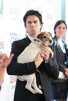 a man in a suit holding a small dog at an awards event with other people around him