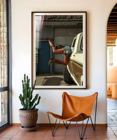 a chair sitting in front of a window next to a potted plant and a framed photograph