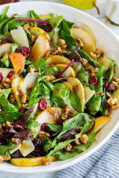 a salad with apples, walnuts and cranberries in a white bowl on a table