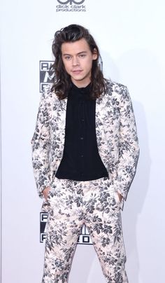 a male in a floral suit and black shirt is posing for a photo on the red carpet