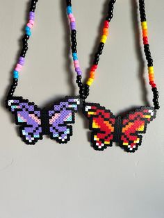 three necklaces made out of beads with colorful butterflies on them hanging from the wall