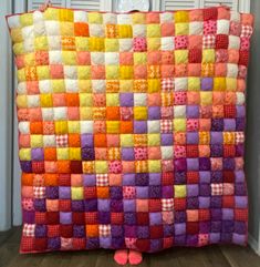 a colorful quilt is hanging on the wall next to a pair of pink slippers