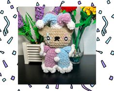 a crocheted teddy bear sitting next to flowers on a table with a frame around it