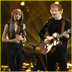 a man and woman singing on stage with microphones in front of them, one holding an acoustic guitar