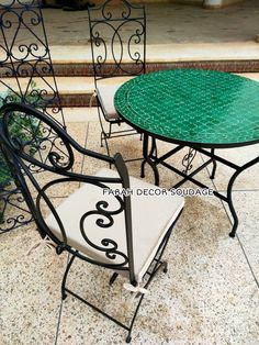 three wrought iron patio furniture set with green glass top table and two white chairs on the ground