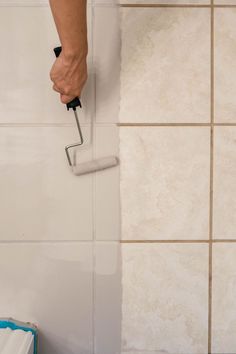 a person is using a paint roller on the wall next to a tiled bathroom floor