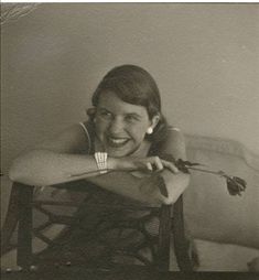 an old black and white photo of a smiling woman sitting on a chair holding a rose