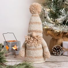 a crocheted teddy bear sitting in front of a christmas tree and other decorations