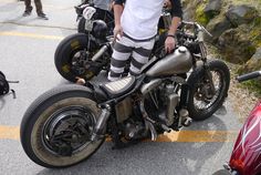 a man standing next to a parked motorcycle on a road with other motorcycles in the background