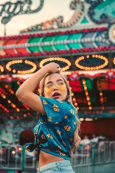 a woman wearing sunglasses standing in front of a carnival ride at night with her arms behind her head