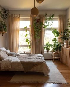 a bedroom with plants hanging from the ceiling and a bed in front of two windows