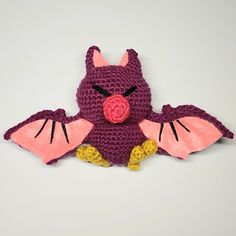 a crocheted bat stuffed animal with large wings and pink nose, sitting on a white surface