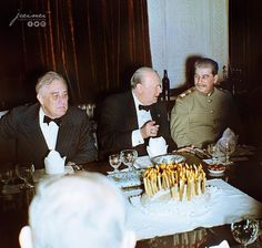 three men sitting at a table with a cake on it and wine glasses in front of them