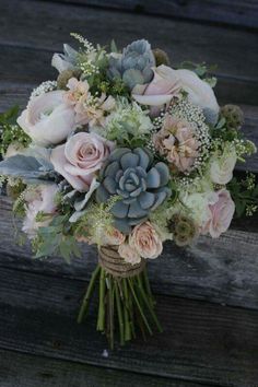 a bridal bouquet with succulents, roses and greenery on a wooden bench