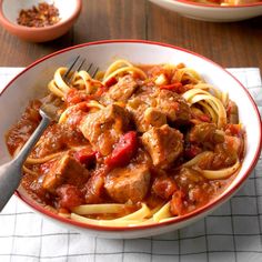 a bowl of pasta with meat and tomato sauce on the side next to a fork