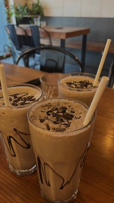 three glasses filled with chocolate milkshakes on top of a wooden table