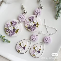 four pairs of earrings with flowers painted on them sitting on a white plate next to green plants