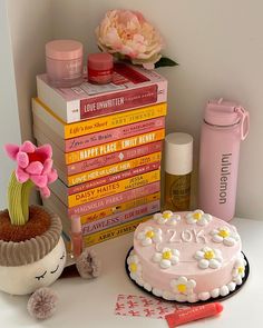 a stack of books next to a cake with flowers on it and a pink flower