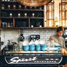 a woman working behind the counter in a coffee shop with blue pots and pans on it