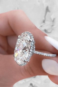 a woman's hand holding an oval shaped diamond ring with diamonds on the band