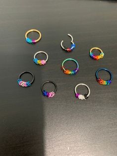 six pairs of rainbow colored hoop earrings on a black surface with one earring in the middle