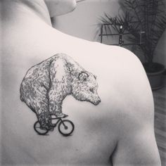 a bear riding a bicycle tattoo on the back of a man