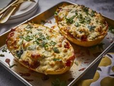 two stuffed peppers with cheese and herbs on a metal tray next to utensils