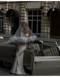 a woman standing next to a car in front of a building with a veil on her head