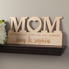 a wooden sign that says mom on top of a shelf next to flowers and a vase