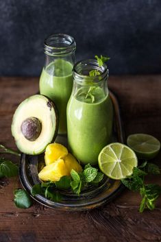 two glass bottles filled with green smoothie next to sliced avocado