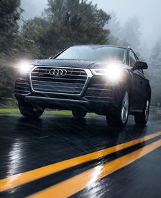 an audi suv driving on a wet road in the rain with its headlights turned down