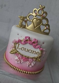 a pink and white cake with gold crown on top that says loucane surrounded by flowers